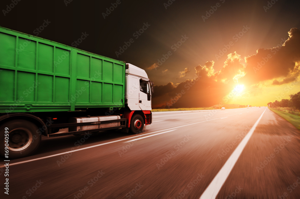 Truck driving fast with the container on the road against sky with sunset