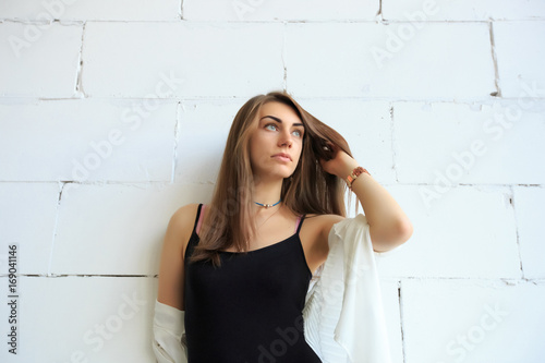 Portrait of trendy young caucasian woman posing near a white brick wall.