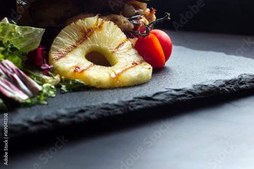 Pineapple ring lies on a black slate surface, in the background a hamburger. photo