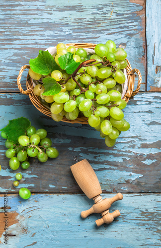 Overhead green grapes in knitted basket on old blue rustic wooden table and cork opener