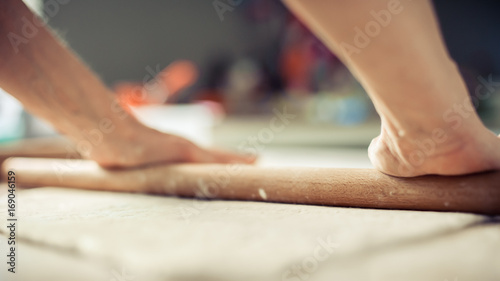 Woman rolling dough on wooden table with wooden rolling pin