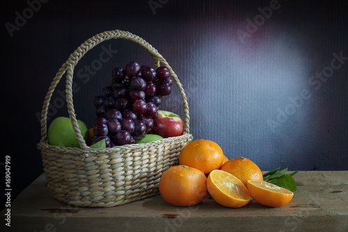 Grapes, apples and oranges  in a in wicker basket on a wooden table, still life style.