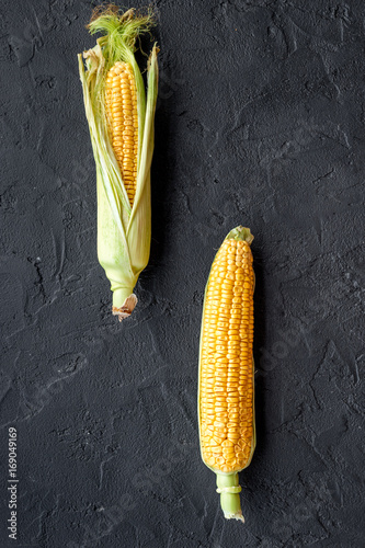 Fotografie Ripe corn on cobs on black stone background top view
