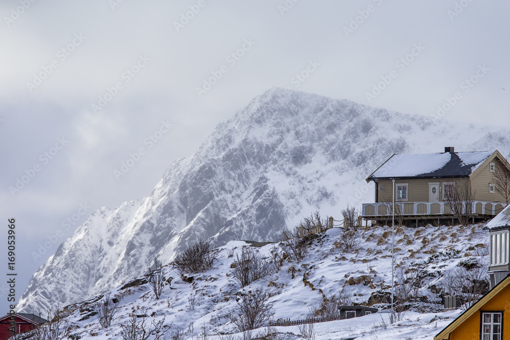 Traditional Norwegian Wooden House in Lofoten Islands Mountain Slope Against Cloudy Sky and Mountain.