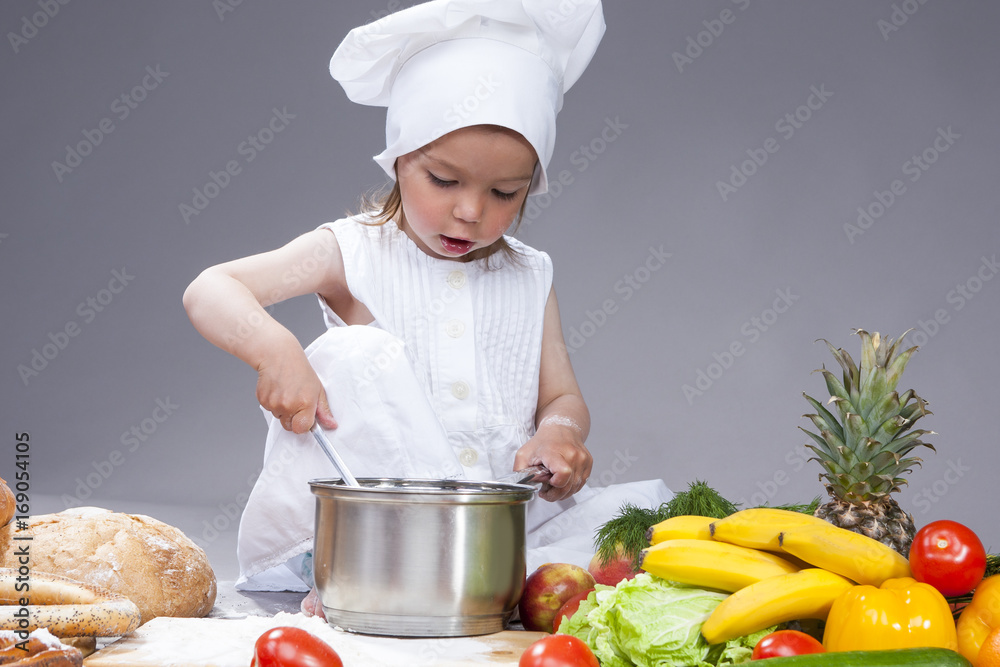 Portrait of Caucasian Little Girl In Cook Uniform Working With Scoop and Saucepan In Studio.Posing Against Gray Background Portrait of Caucasian Little Girl In Cook Uniform Working With Scoop and Saucepan In Studio.Posing Against Gray Background
