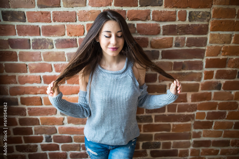 Beautiful young woman in casual wear hands play with hair smiling, standing against white brick wall Beautiful young woman in casual wear hands play with hair smiling, standing against white brick wall