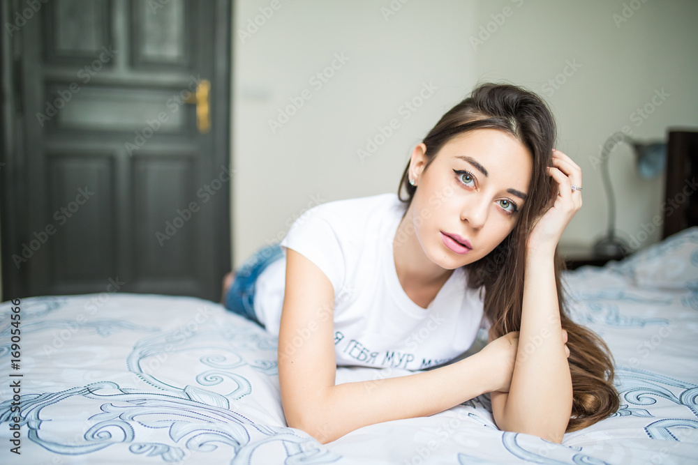 Young woman looking at camera and smiling while lying on the bed at home Young woman looking at camera and smiling while lying on the bed at home