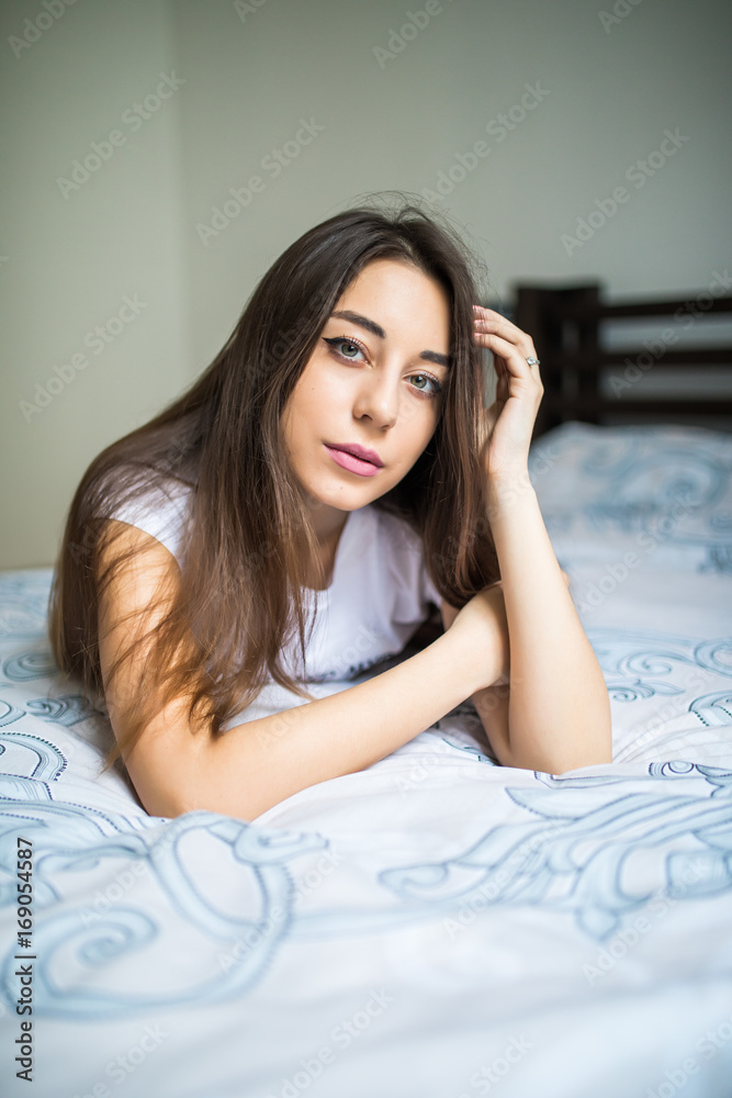 Young woman looking at camera and smiling while lying on the bed at home Young woman looking at camera and smiling while lying on the bed at home