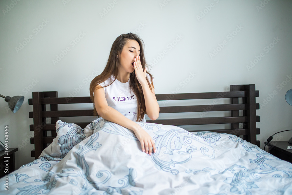 Young woman sitting on the bed and yawning at home
