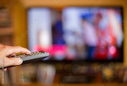 A woman switches on a TV with a remote control
