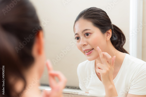 smiling young woman applying face cream on finger