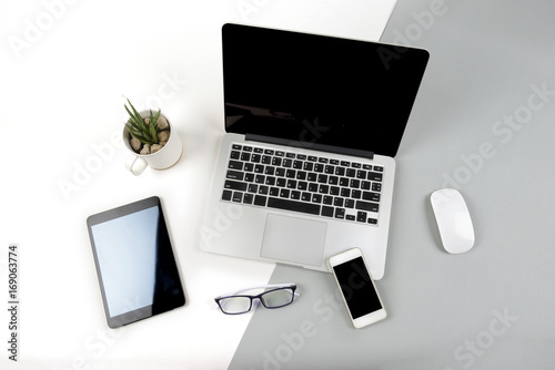 Office table with laptop computer, digital tablet and mobile phone on modern two tone (white and grey) background.