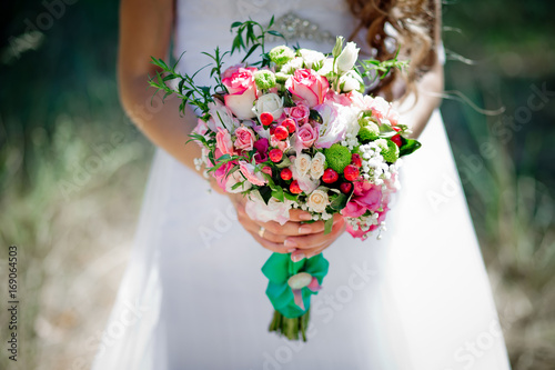 Fototapeta Naklejka Na Ścianę i Meble -  A bridal bouquet with roses, eustoma, berries in the bride's hands. Floristic composition.