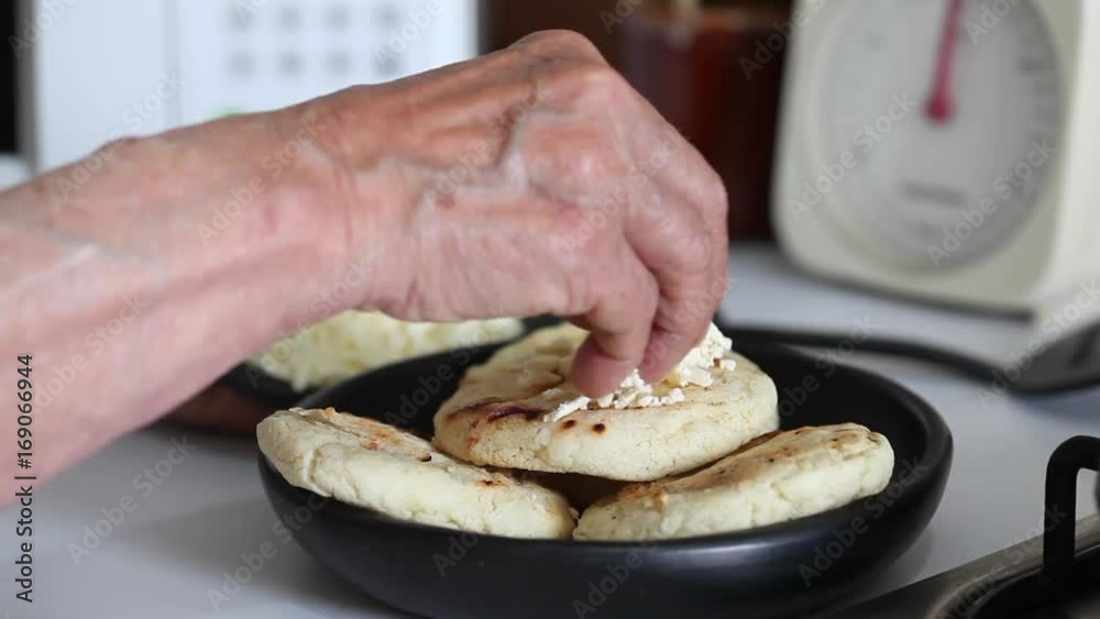 Hands of a senior woman adding shredded cheese to a roasted arepa Hands of a senior woman adding shredded cheese to a roasted arepa