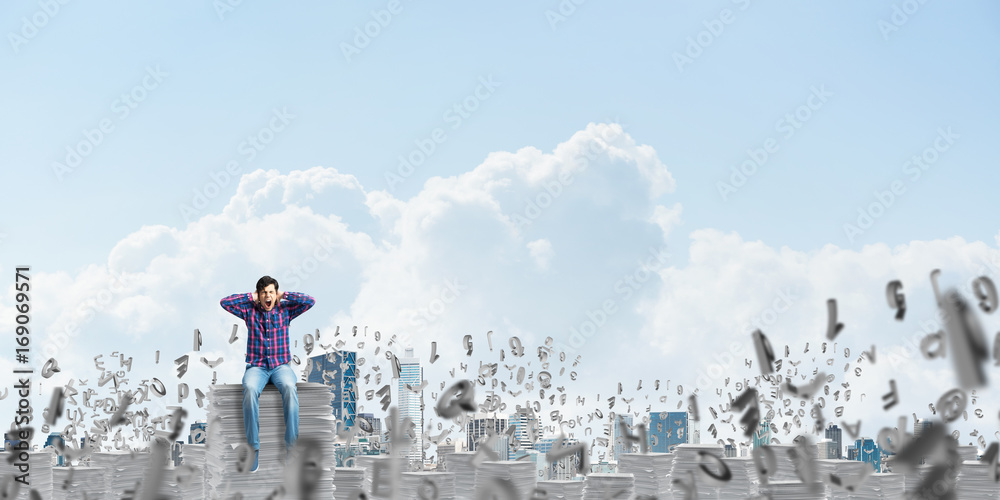 Attractive man sitting on pile of paper documents.