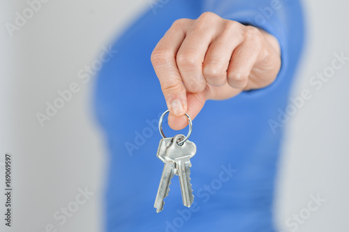 Woman holding home keys in front of her body. Focus on foreground