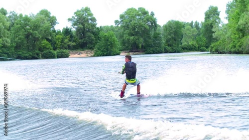 Wakeboarder doing tricks HD wakeboarding slow-motion video. Man rides behind boat and jumps somersault flip on waves. Water extreme sport.
