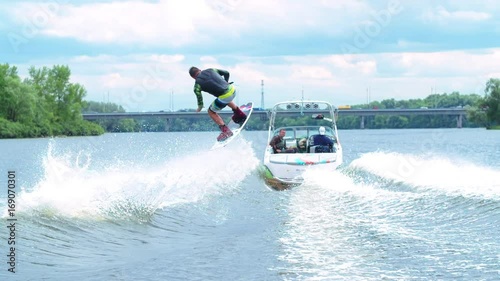 Wakeboarder doing tricks HD wakeboarding slow-motion video. Man rides behind boat and jumps somersault flip on waves. Water extreme sport.