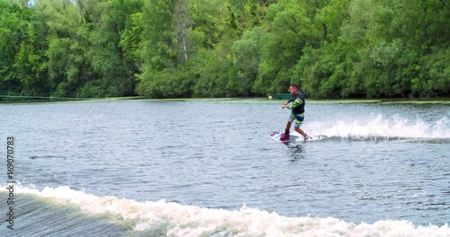 Wakeboarder doing tricks 4k wakeboarding video. Man rides behind boat and jumps somersault flip on waves. Water extreme sport.