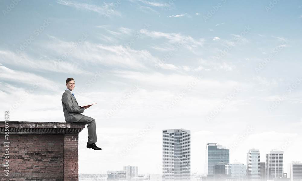 Man on roof edge reading book and cityscape at background Man on roof edge reading book and cityscape at background