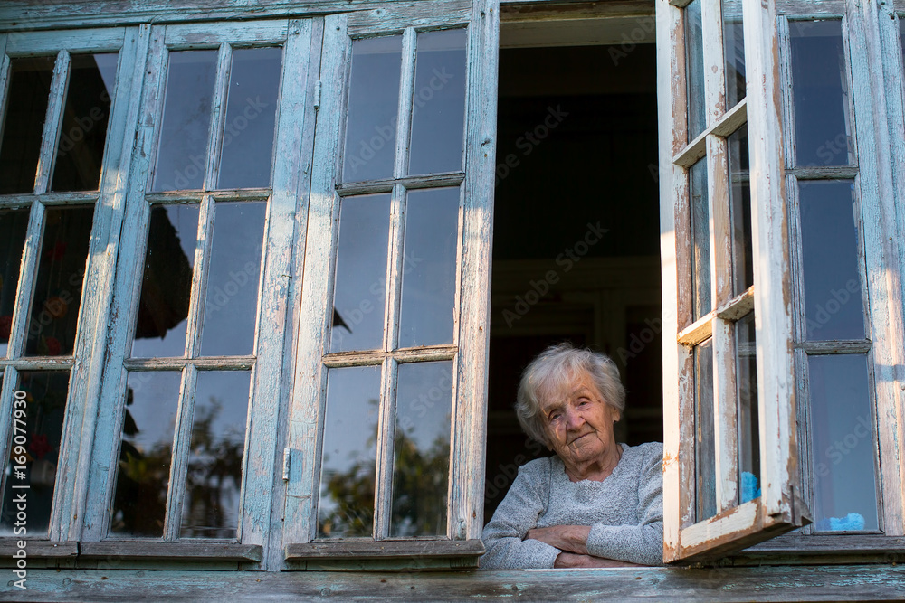 Grandmother, an elderly woman looks from the window of the farmhouse. Grandmother, an elderly woman looks from the window of the farmhouse.
