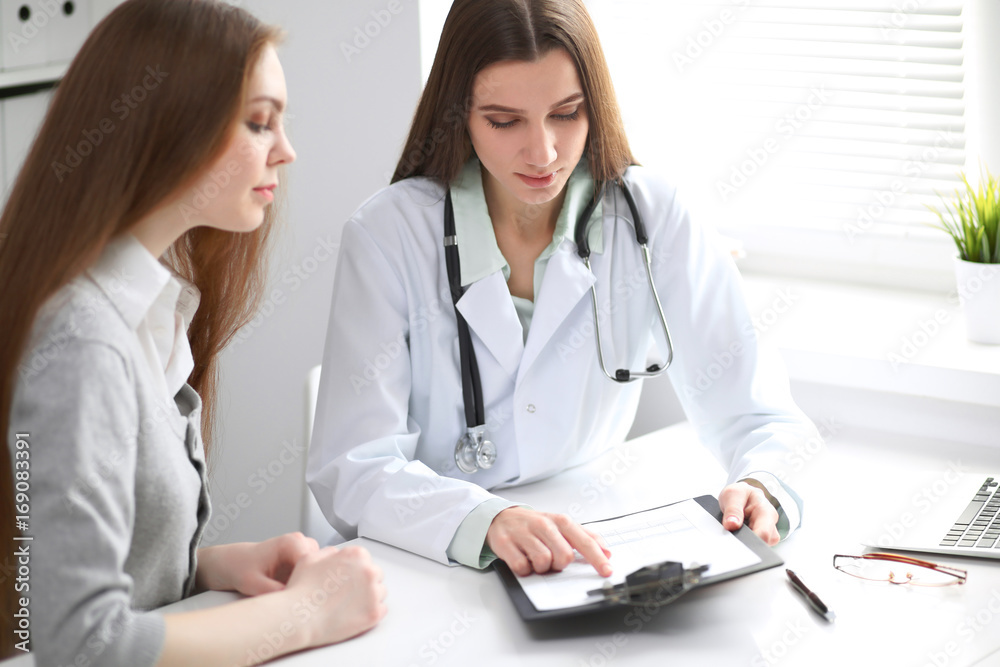 Female doctor having a talk with her patient while sitting at the table near the window in hospital. Physician is ready to help patient. Medicine and health care concept Female doctor having a talk with her patient while sitting at the table near the window in hospital. Physician is ready to help patient. Medicine and health care concept