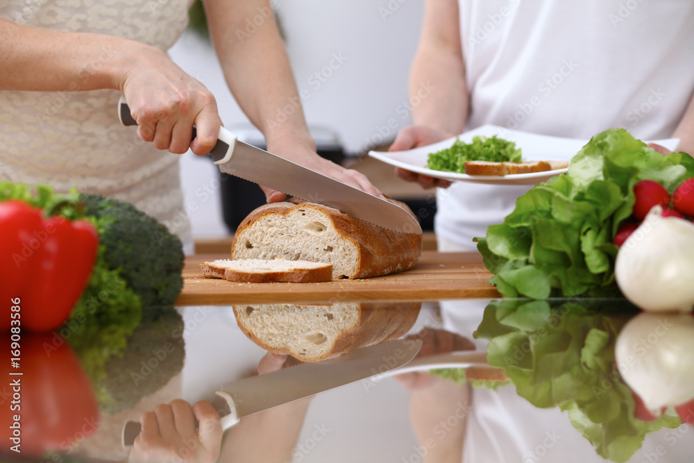 Close-up of human hands slicing bread in a kitchen. Friends having fun while preparing fresh salad. Chef cook represent culinary masterclass. Vegetarian, healthy meal and friendship concept