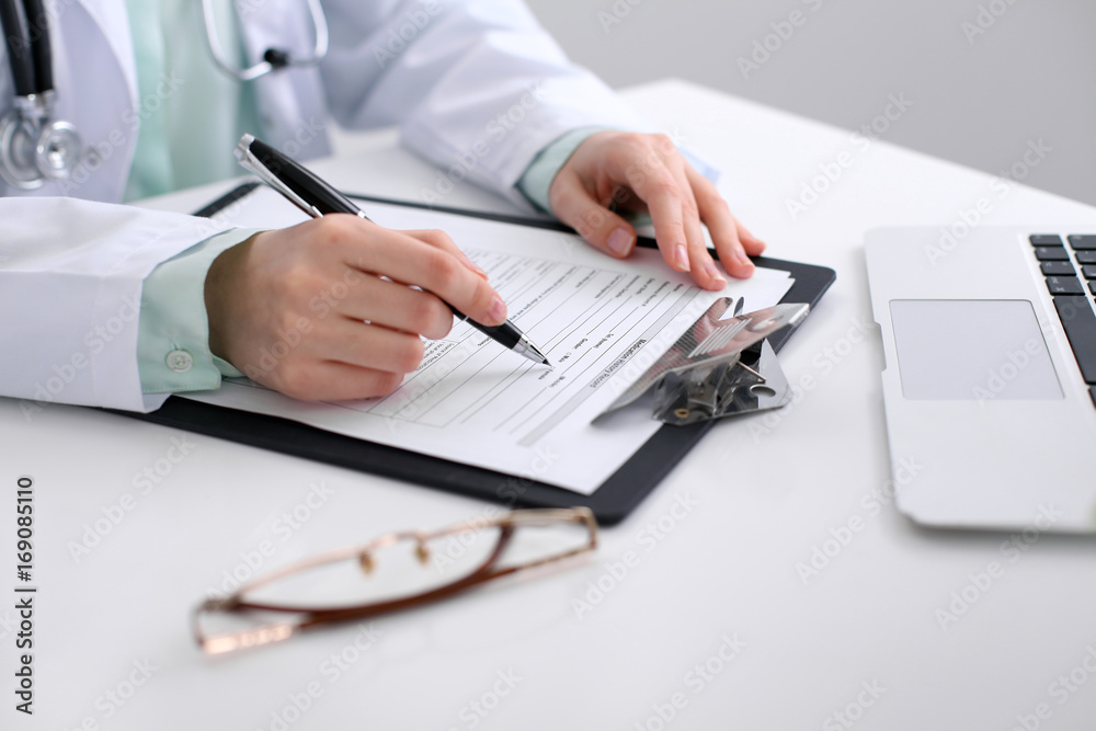 Close-up of a female doctor filling out application form , sitting at the table in the hospital Close-up of a female doctor filling out application form , sitting at the table in the hospital