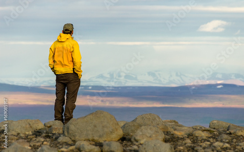 Man standing on mountain, looking relaxed towards snowy mountain range.