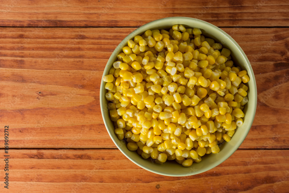 Flat lay above bowl with cooked corn on the wooden table Flat lay above bowl with cooked corn on the wooden table