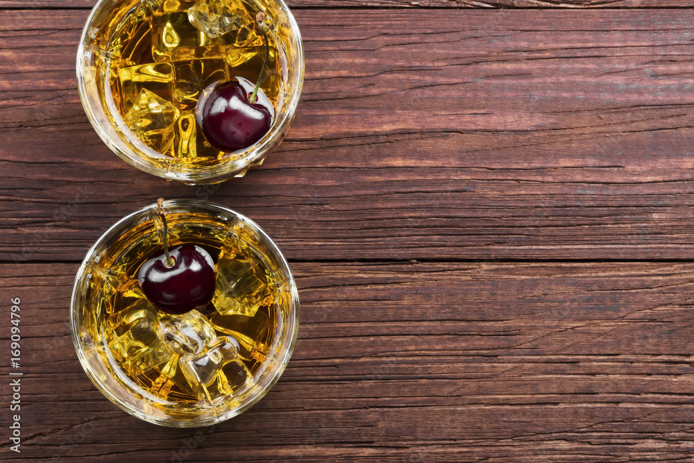 Cocktail from whisky with cherry in two glasses on a wooden background. Top view, copy space. Food background