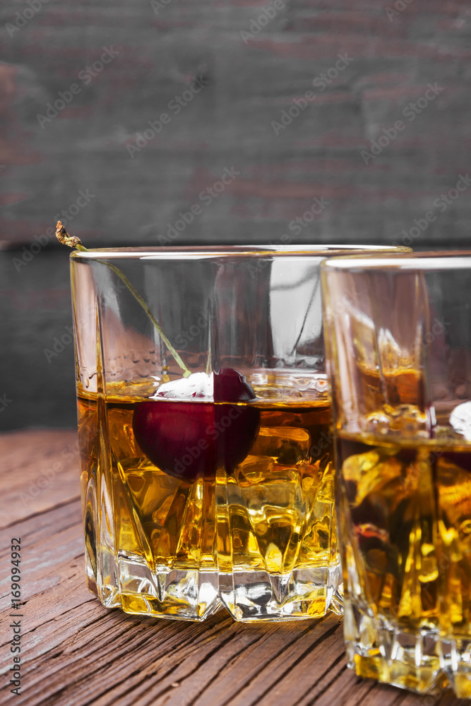 Cocktail from whisky with cherry in two glasses on a wooden background