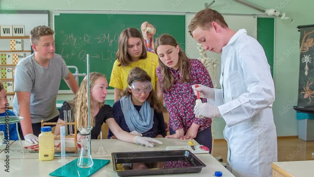 A boy is about to do an experiment for his classmates in a chemistry class. They are carefully watching him. A boy is about to do an experiment for his classmates in a chemistry class. They are carefully watching him.