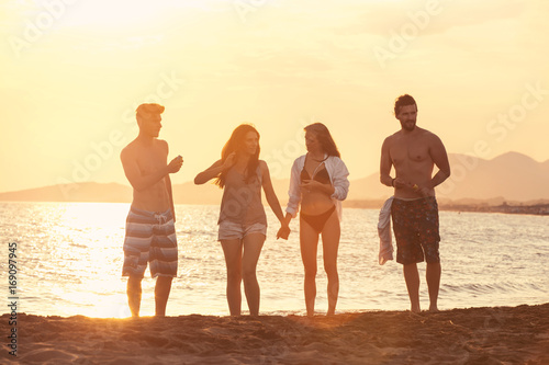 Group of happy people walkin on beautiful beach in summer sunset