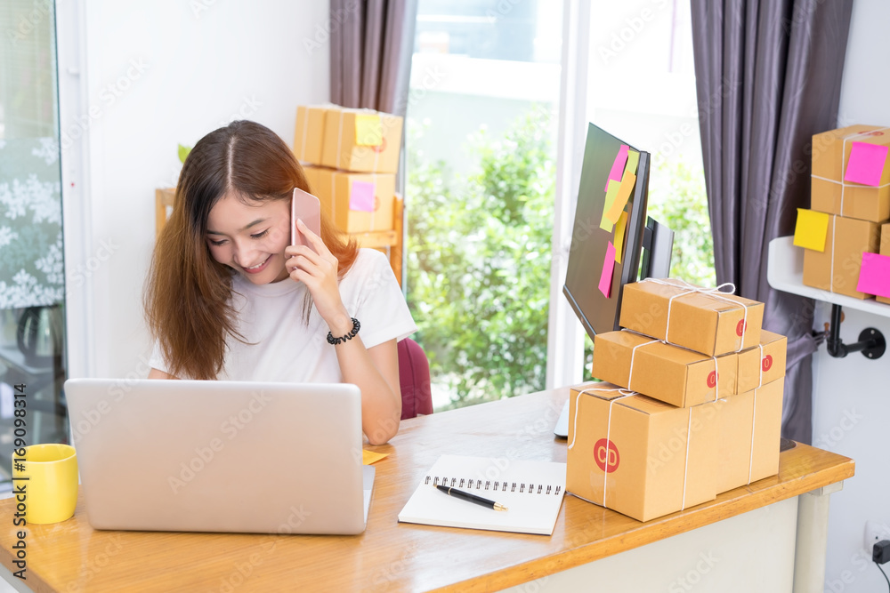 Young asian girl freelancer business private working at home office using mobile taking post it paper with laptop, note, coffee, packaging delivery online market on purchase orders to customer.