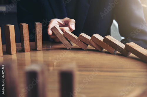 Close up of businessman hand Stopping Falling wooden Dominoes effect from continuous toppled or risk, strategy and successful intervention concept for business