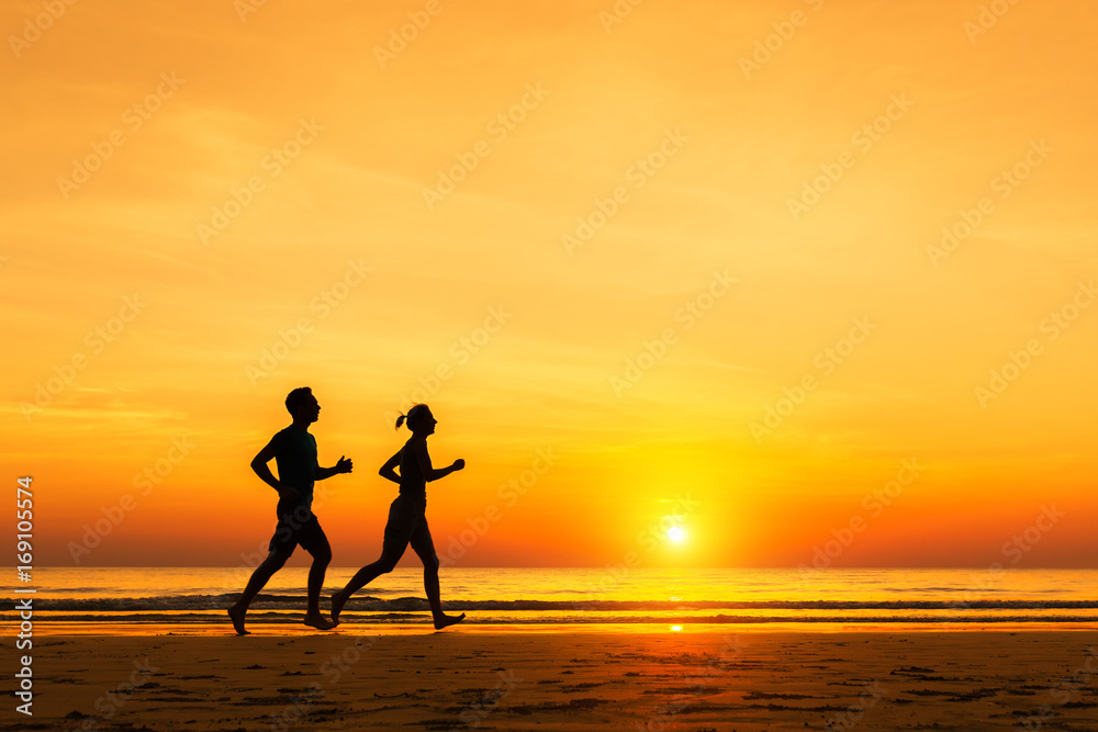 Silhouette of active sporty couple running on the beach, sunset