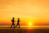 Silhouette of active sporty couple running on the beach, sunset