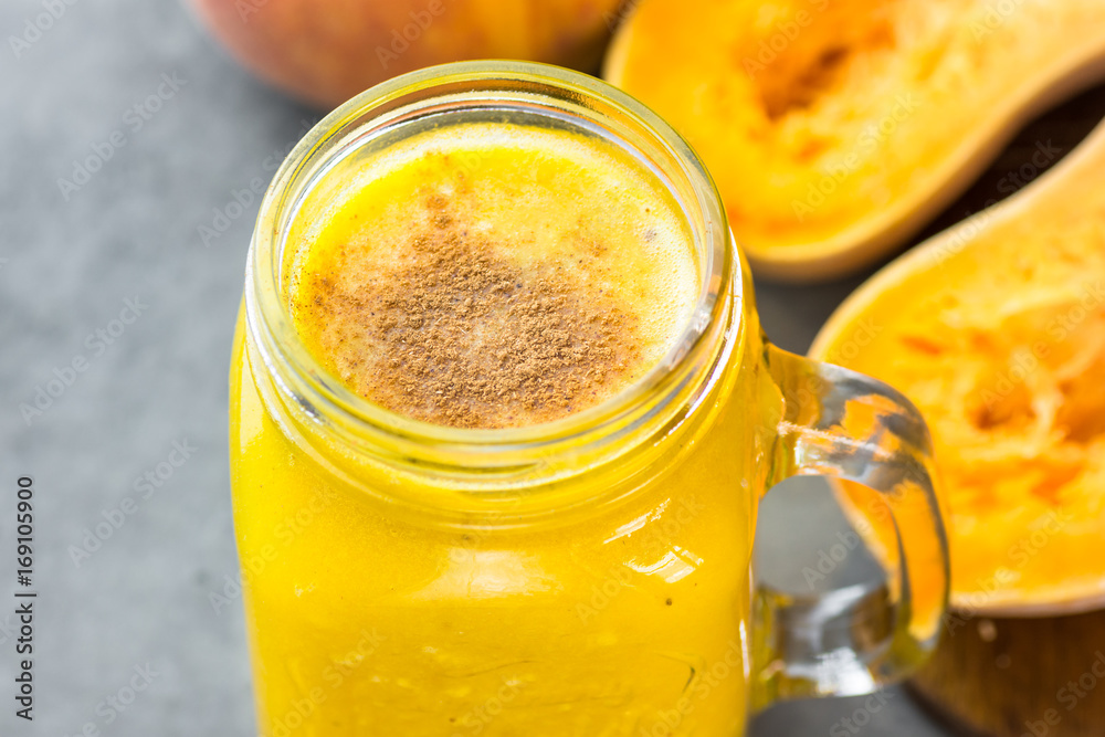 Glass mason jar with raw pumpkin butternut squash smoothie with peaches, bananas, cinnamon, spices. Ingredients on dark stone table. Bight colors, close up.