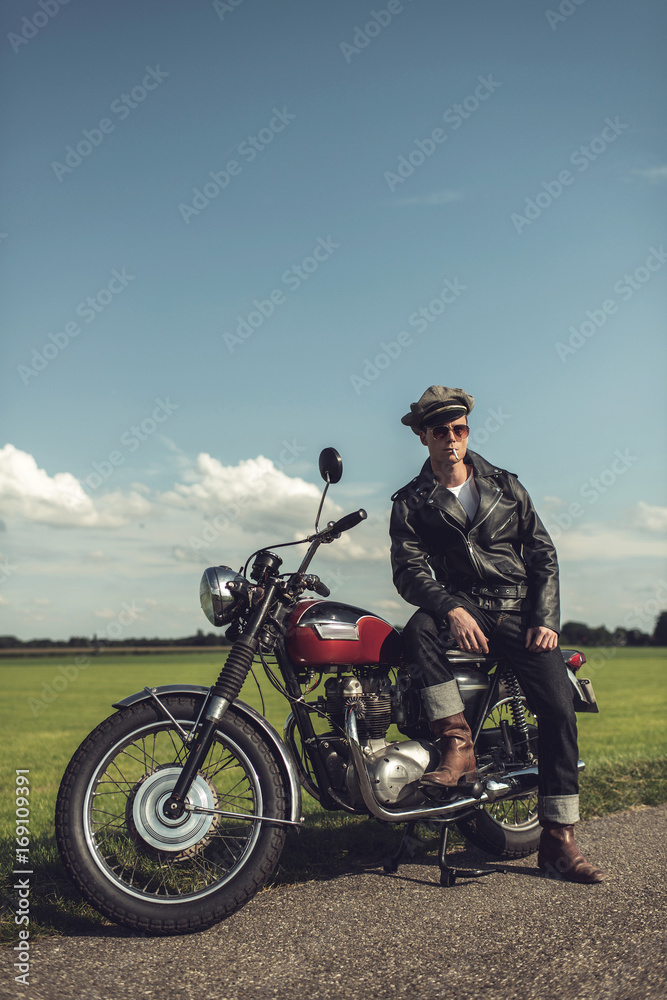 Obraz premium Vintage motorcyclist having a break along rural road in summer.