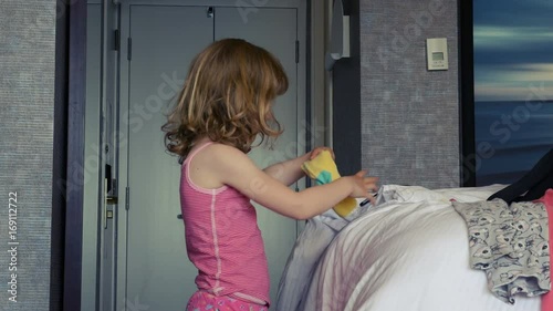 A little girl gets dressed. She tries to put on a yellow sock. Long shot.