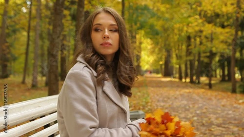 Smiling woman keeps a bunch of yellow leaves and waves to her honey