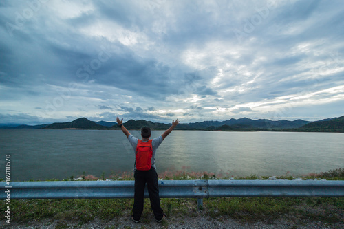 An orange backpacker travels to watch the sunset at the Pranburi Dam. Prachuap Khiri Khan, Thailand © Tavaris