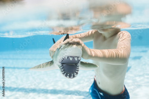 Boy (6-7) playing with toy shark in swimming pool