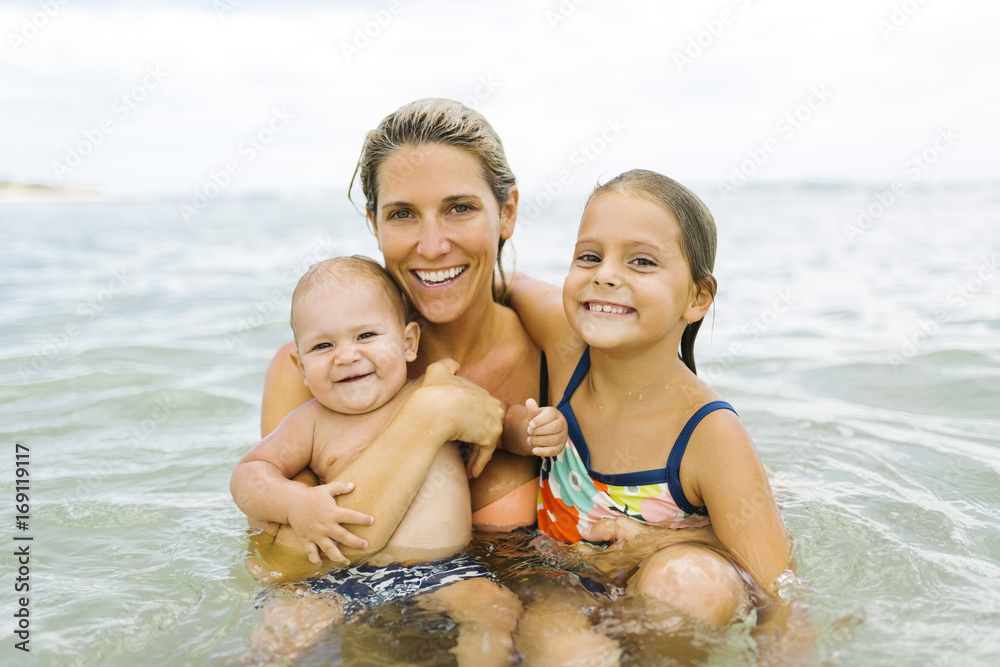 Mother and children (6-7, 12-17 months) embracing in sea Mother and children (6-7, 12-17 months) embracing in sea