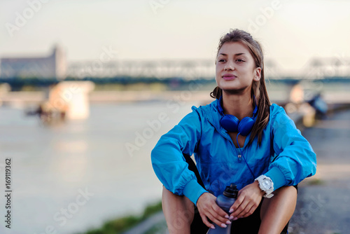 Young woman jogger resting drinking water by the river