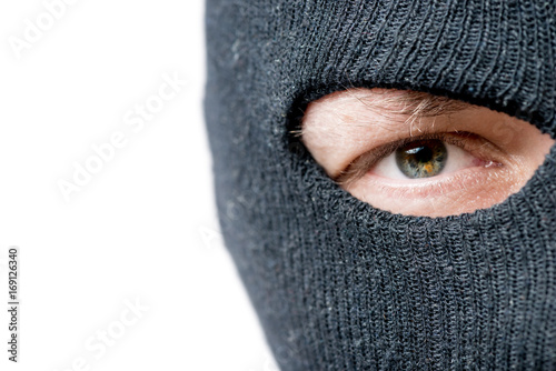 Close-up of the eyes of the criminal whose face is covered by a black mask and the space on the left