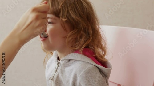 Mom gives the little girl a medicine. Child drinks sweet syrup and smiles