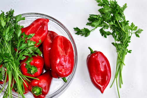 Raw red organic peppers with bunch of aromatic green spice parsley in a glass bowl ready to cook with isolated on white