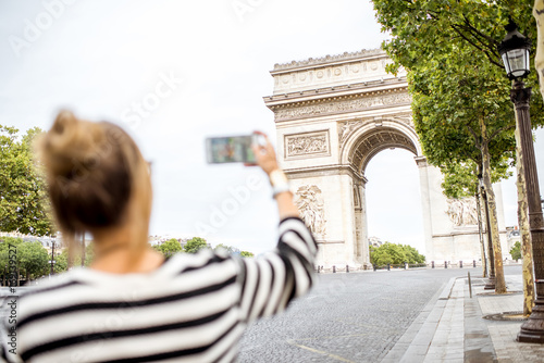 Young woman tourist photographing with phone famous triumphal arch in Paris. Image focused on the background, woman is out of focus © rh2010